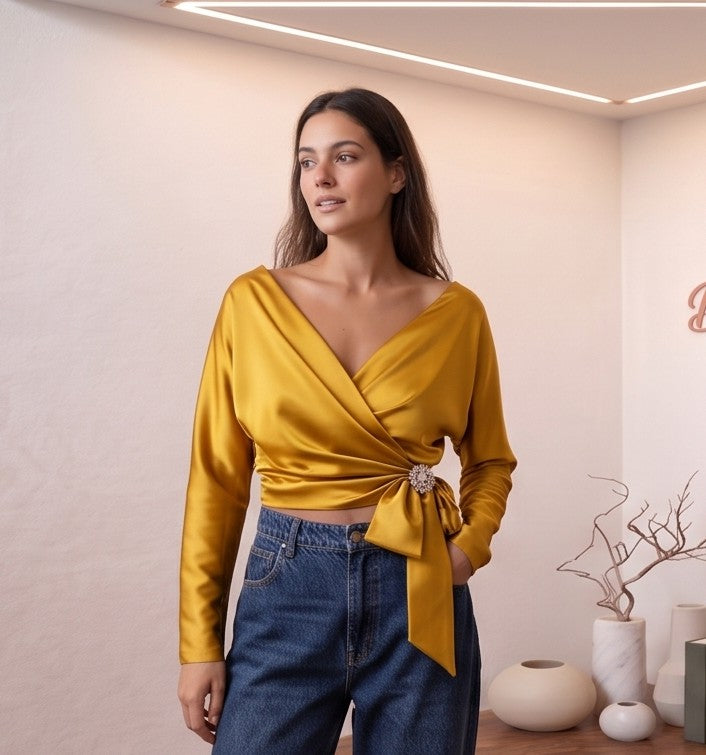 Blusa de satén de seda con diseño cruzado, escote en V y lazada lateral con detalle de broche. Disponible en varios colores: amarillo vibrante, azul cielo, blanco roto y champán. Manga larga y corte elegante y sofisticado.