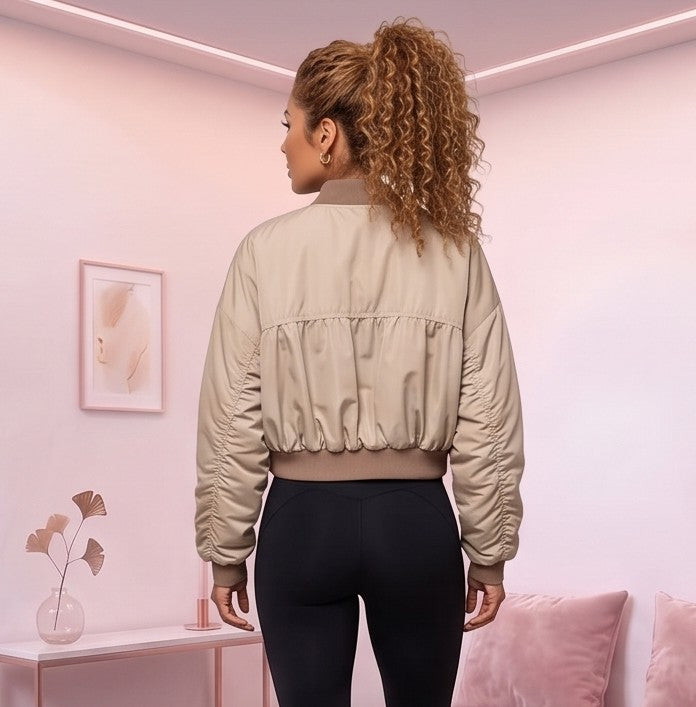 Chaqueta bomber corta de mujer color caqui claro con cuello redondo acanalado, cremallera metálica frontal, mangas con fruncido y pretina elástica entallada en la cintura, fotografiada en estudio con vista frontal y trasera