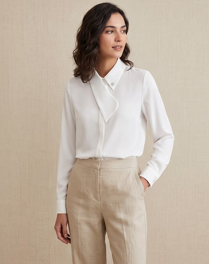 Blusa blanca de manga larga para mujer con solapa asimétrica cruzada, cuello camisero elegante y detalle de botón joya brillante.