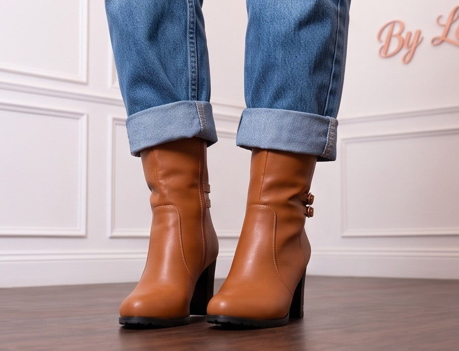 Botas de media caña para mujer en polipiel PU con tacón ancho alto y detalles metálicos dorados en la base del tacón. Diseño de puntera redonda con doble tira lateral decorativa, hebillas doradas redondas y cierre de cremallera interior. Disponibles en color negro, blanco y camel