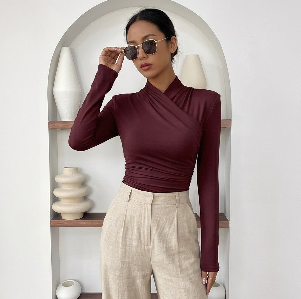 Camiseta ajustada de manga larga para mujer con cuello alto cruzado y detalle de fruncido lateral, disponible en tonos burdeos, azul oscuro, verde, rojo, negro, blanco, marrón y beige.