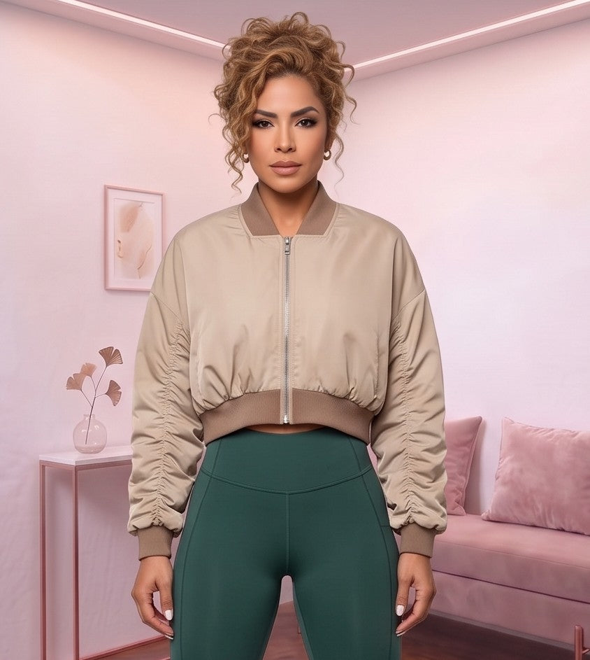 Chaqueta bomber corta de mujer color caqui claro con cuello redondo acanalado, cremallera metálica frontal, mangas con fruncido y pretina elástica entallada en la cintura, fotografiada en estudio con vista frontal y trasera