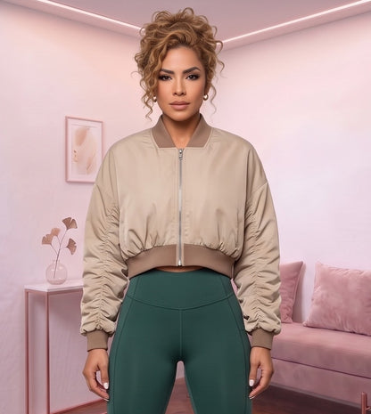 Chaqueta bomber corta de mujer color caqui claro con cuello redondo acanalado, cremallera metálica frontal, mangas con fruncido y pretina elástica entallada en la cintura, fotografiada en estudio con vista frontal y trasera