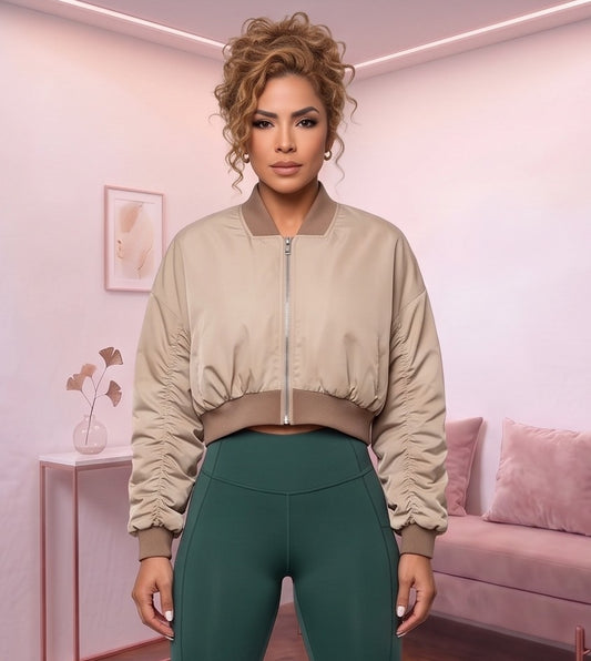Chaqueta bomber corta de mujer color caqui claro con cuello redondo acanalado, cremallera metálica frontal, mangas con fruncido y pretina elástica entallada en la cintura, fotografiada en estudio con vista frontal y trasera