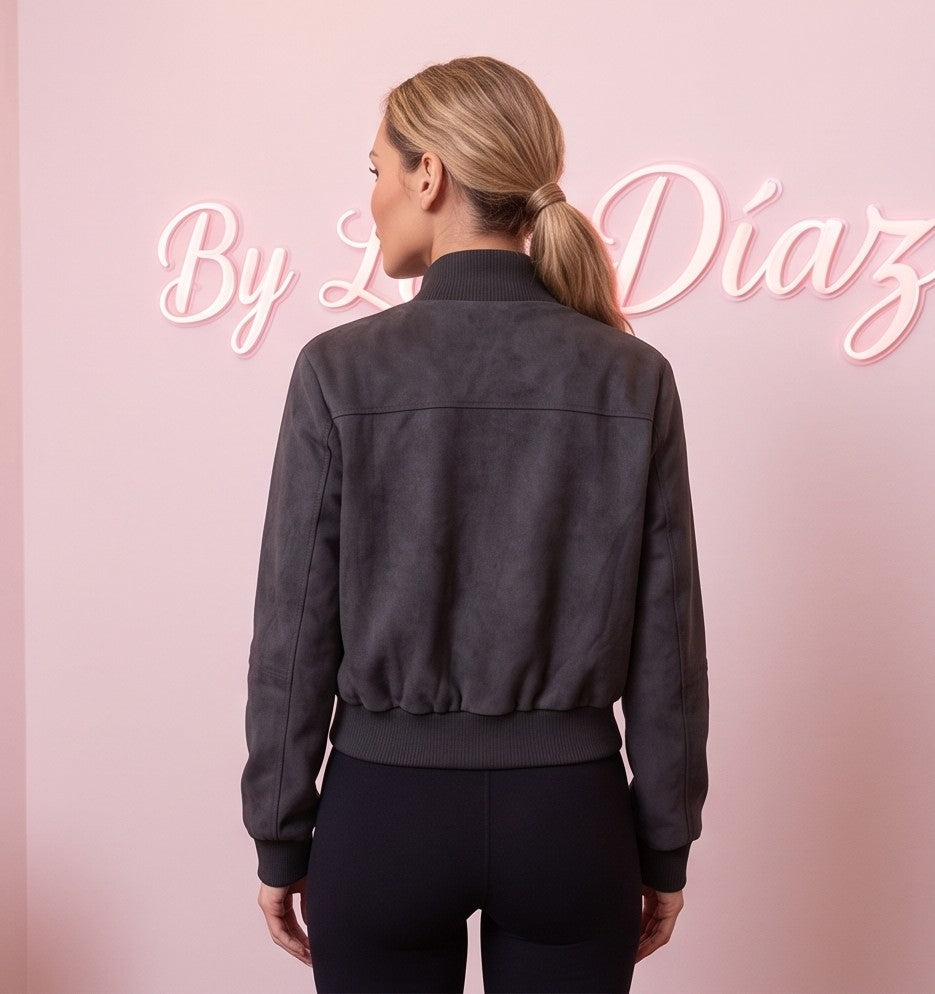 Chaqueta corta estilo bomber para mujer con cuello alto elástico acanalado, cremallera metálica central, dos bolsillos con solapa en el pecho y bolsillos laterales de cremallera, confeccionada en tejido de efecto antelina suave disponible en tonos caqui y gris oscuro