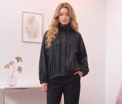 Chaqueta estilo bomber negra de corte oversized con cuello alto alzado, cierre de cremallera frontal y mangas largas abullonadas con puños elásticos, fabricada en tejido ligero de poliéster para un look urbano y casual.