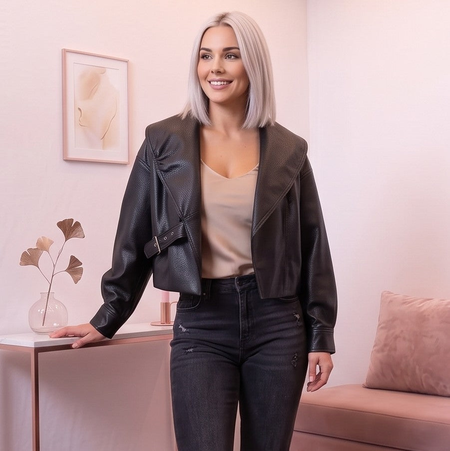 Detalle del dobladillo, costuras y acabado de Chaqueta corta de piel sintética en color negro para mujer, con solapa ancha, cierre cruzado con hebilla lateral ajustable, mangas largas con puños abotonados y diseño moderno de estilo motero casual.
