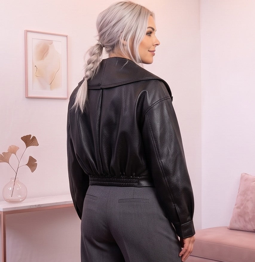 Detalle del dobladillo, costuras y acabado de Chaqueta corta de piel sintética en color negro para mujer, con solapa ancha, cierre cruzado con hebilla lateral ajustable, mangas largas con puños abotonados y diseño moderno de estilo motero casual.

