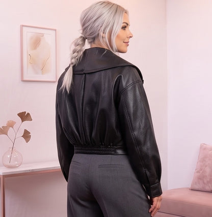 Detalle del dobladillo, costuras y acabado de Chaqueta corta de piel sintética en color negro para mujer, con solapa ancha, cierre cruzado con hebilla lateral ajustable, mangas largas con puños abotonados y diseño moderno de estilo motero casual.

