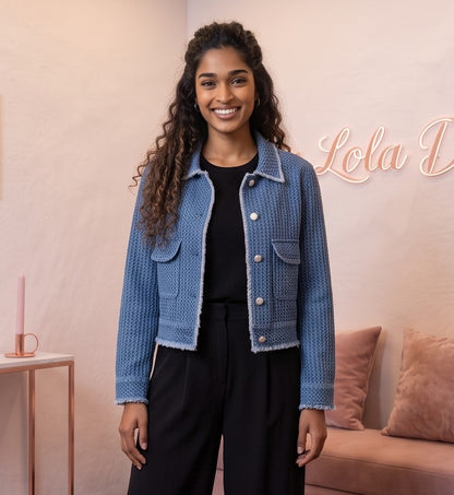 Chaqueta corta de mujer en tejido texturizado azul denim con bolsillos frontales de parche, cuello clásico y botones blancos estilo joya, ideal para un look casual y urbano.