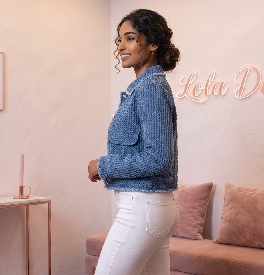 Chaqueta corta de mujer en tejido texturizado azul denim con bolsillos frontales de parche, cuello clásico y botones blancos estilo joya, ideal para un look casual y urbano.