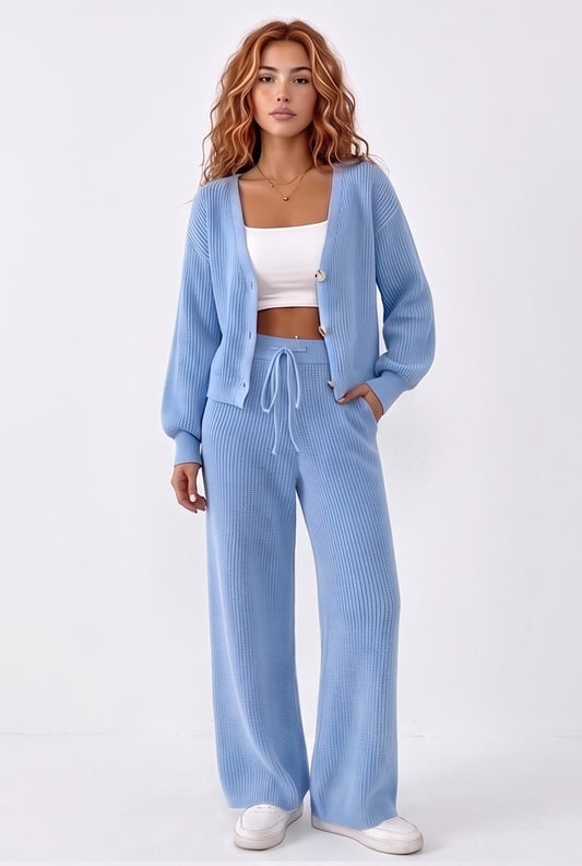 Conjunto de dos piezas de punto acanalado para mujer compuesto por cárdigan de manga larga con cuello en pico y botones frontales, a juego con pantalón largo holgado de tiro alto y cintura elástica con cordón ajustable; disponible en color azul cielo, crema albaricoque y negro.