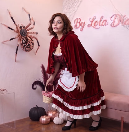 Disfraz de Caperucita Roja estilo gótico y fantasía para mujer, compuesto por vestido de terciopelo rojo vino con corpiño a rayas, delantal blanco con volantes, falda acampanada con ribete blanco y capa corta a juego con capucha amplia con fruncidos.