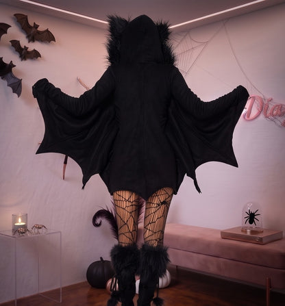 Disfraz enterizo de murciélago para mujer en tejido negro suave tipo pana con cremallera frontal, mangas murciélago que simulan alas extendidas y capucha afelpada con orejas puntiagudas.