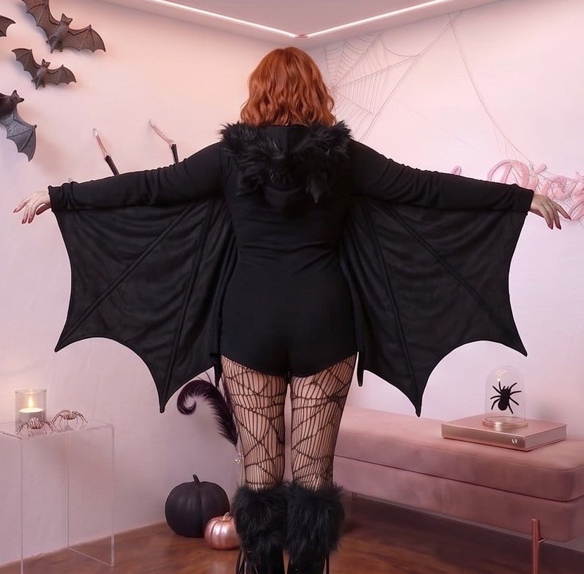 Disfraz enterizo de murciélago para mujer en tejido negro suave tipo pana con cremallera frontal, mangas murciélago que simulan alas extendidas y capucha afelpada con orejas puntiagudas.
