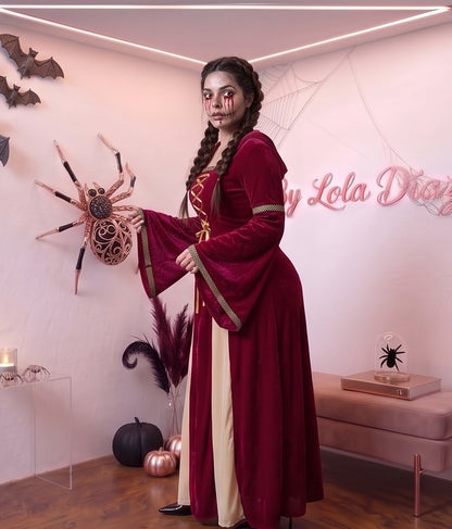 Disfraz medieval y gótico de mujer con vestido largo hasta los pies en tejido de terciopelo rojo burdeos, detalle frontal drapeado en tono crema y corsé con lazos dorados cruzados, mangas largas acampanadas acampanadas con ribetes dorados y capucha holgada integrada, ideal para caracterización teatral, temática de época y Halloween.