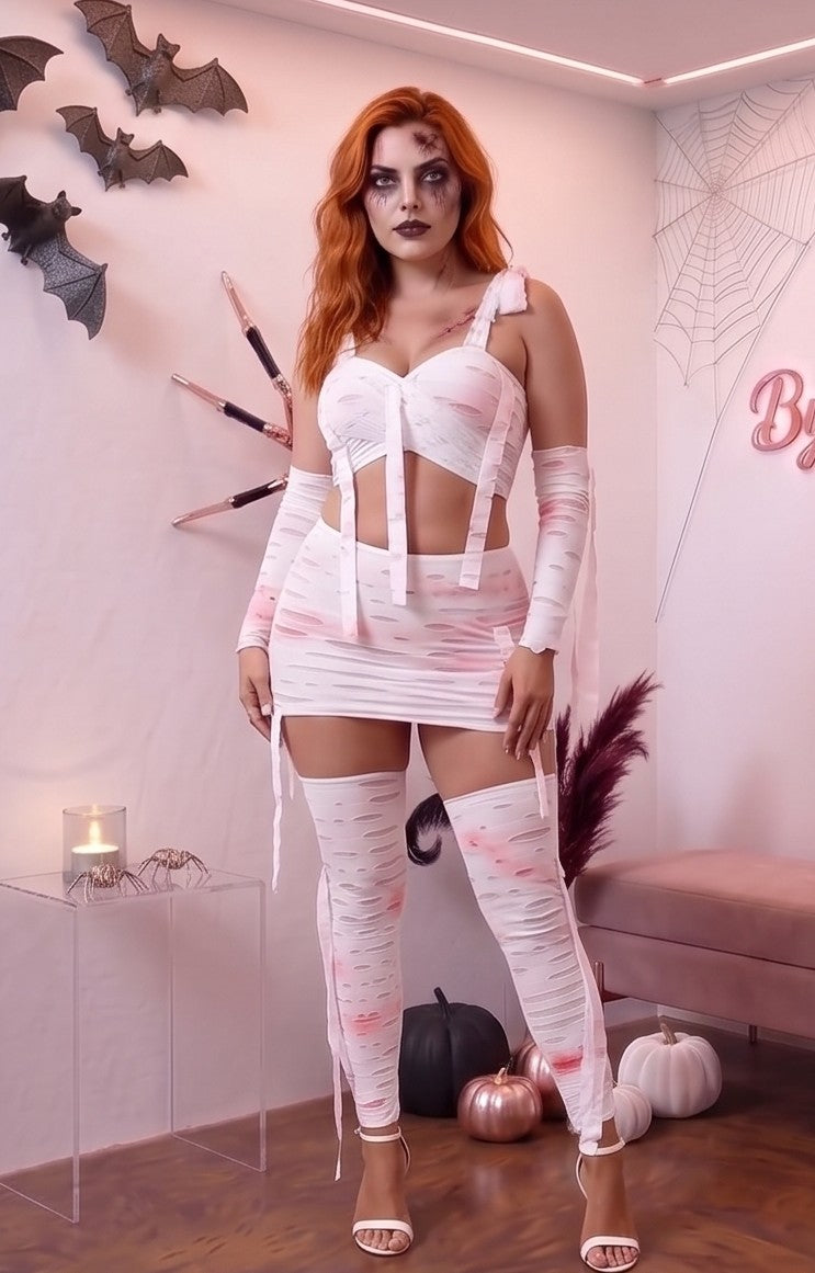 Disfraz de momia para mujer de cuatro piezas en tela elástica blanca con efecto de tiras desgarradas, roturas y manchas de sangre artificial rosa y roja. El conjunto incluye un crop top cruzado con tirantes ajustables, falda corta a juego con cintas colgantes, mangas largas y calentadores cubrepiés a juego sobre fondo de estudio de Halloween.