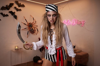 Disfraz de pirata para mujer compuesto por un mono corto con blusa blanca de escote acordonado y volantes, pantalón corto a rayas verticales blancas y negras, fajín rojo anudado a la cintura y pañuelo bandana para la cabeza a rayas coordinadas