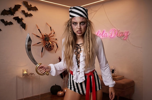 Disfraz de pirata para mujer compuesto por un mono corto con blusa blanca de escote acordonado y volantes, pantalón corto a rayas verticales blancas y negras, fajín rojo anudado a la cintura y pañuelo bandana para la cabeza a rayas coordinadas