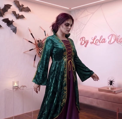 Disfraz de bruja medieval inspirado en Winifred Sanderson con vestido largo en dos piezas simuladas: túnica exterior de terciopelo verde esmeralda con cuello alzado, mangas acampanadas con ribetes dorados y bordados rúnicos en el pecho, sobre falda interior fluida en tono morado púrpura con corsé ajustable de cordones amarillos.