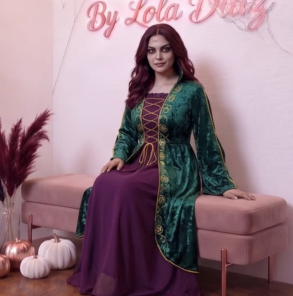 Disfraz de bruja medieval inspirado en Winifred Sanderson con vestido largo en dos piezas simuladas: túnica exterior de terciopelo verde esmeralda con cuello alzado, mangas acampanadas con ribetes dorados y bordados rúnicos en el pecho, sobre falda interior fluida en tono morado púrpura con corsé ajustable de cordones amarillos.