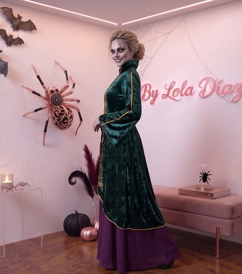 Disfraz de bruja medieval inspirado en Winifred Sanderson con vestido largo en dos piezas simuladas: túnica exterior de terciopelo verde esmeralda con cuello alzado, mangas acampanadas con ribetes dorados y bordados rúnicos en el pecho, sobre falda interior fluida en tono morado púrpura con corsé ajustable de cordones amarillos.