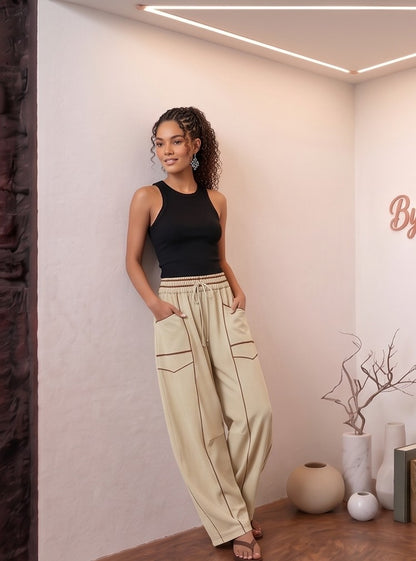 Pantalón fluido estilo bombacho wide leg para mujer con cintura elástica de cordón ajustable, costuras vistas en contraste y bolsillos cargo laterales geométricos, disponible en 8 colores: amarillo pastel, azul celeste, verde esmeralda, blanco tiza, beige arena, marrón chocolate, azul marino y negro con pespuntes dorados
