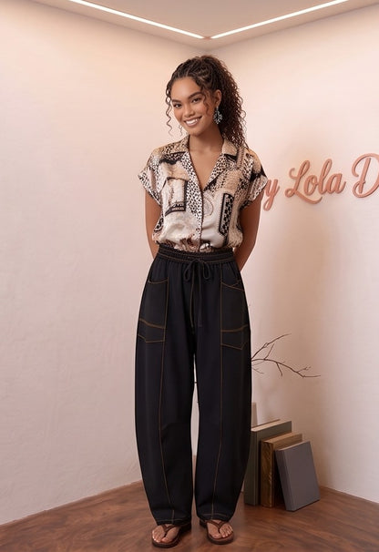 Pantalón fluido estilo bombacho wide leg para mujer con cintura elástica de cordón ajustable, costuras vistas en contraste y bolsillos cargo laterales geométricos, disponible en 8 colores: amarillo pastel, azul celeste, verde esmeralda, blanco tiza, beige arena, marrón chocolate, azul marino y negro con pespuntes dorados