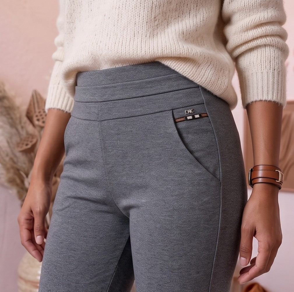 pantalón gris ajustado con bolsillos decorados con detalles metálicos. A la derecha, lleva un pantalón negro similar, también con bolsillos metálicos. Ambos pantalones se ajustan a la cintura y llegan hasta los tobillos.