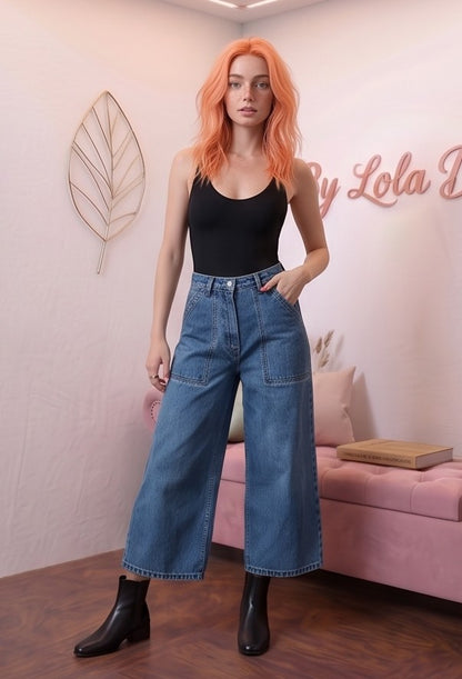 Pantalón vaquero azul para mujer de estilo urbano y casual. Diseño de pierna ancha y tiro alto, largo tobillero 9/10, con distintivos bolsillos delanteros cuadrados tipo parche y cierre clásico de botón. Tejido denim liso.