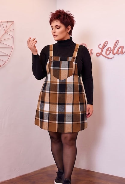 Peto vestido pichi corto para mujer curvy en estampado clásico de cuadros escoceses con corte línea A, tirantes anchos con botones y bolsillo frontal plastrón, confeccionado en mezcla de poliéster cálido, disponible en tonos verde botella, marrón camel y gris con negro sobre jersey de punto.