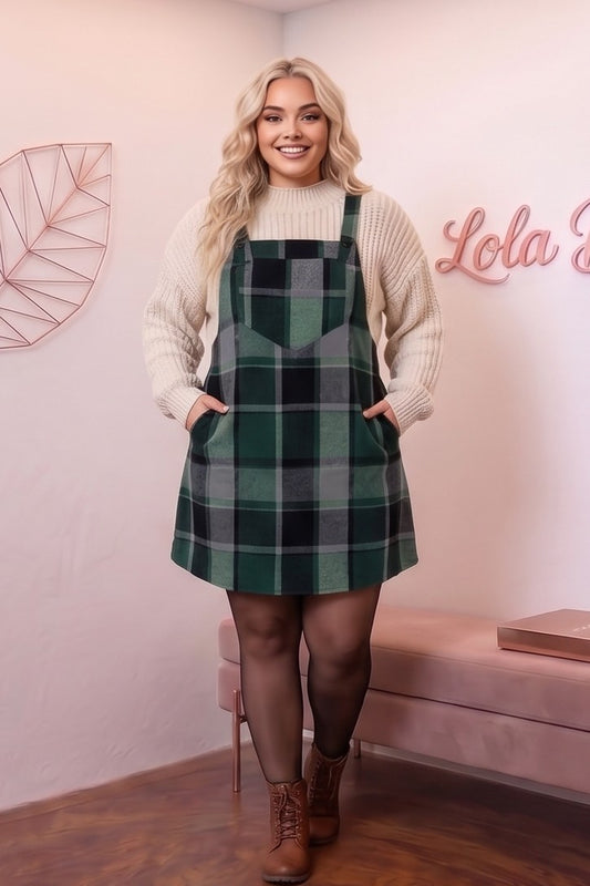 Peto vestido pichi corto para mujer curvy en estampado clásico de cuadros escoceses con corte línea A, tirantes anchos con botones y bolsillo frontal plastrón, confeccionado en mezcla de poliéster cálido, disponible en tonos verde botella, marrón camel y gris con negro sobre jersey de punto.