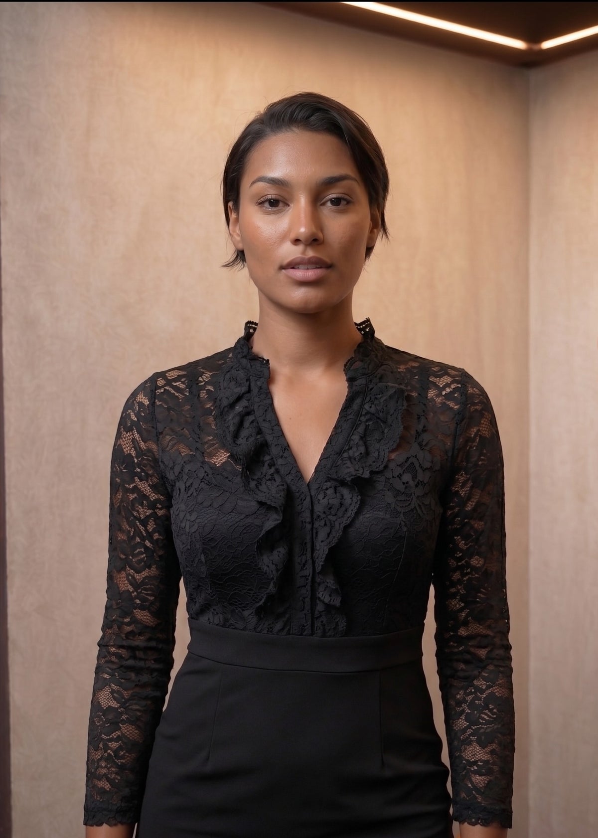 vestido corto de color negro que cuenta con un cuerpo de encaje floral con transparencias en las mangas largas y el cuello V con volantes, cinturilla definida y falda lisa ajustada elegante