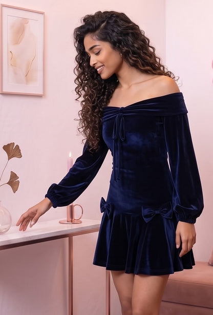 Vestido corto de terciopelo azul marino de corte evasé con escote bardot de hombros descubiertos, mangas largas abullonadas tipo farol y detalle de lazos en cadera y pecho.