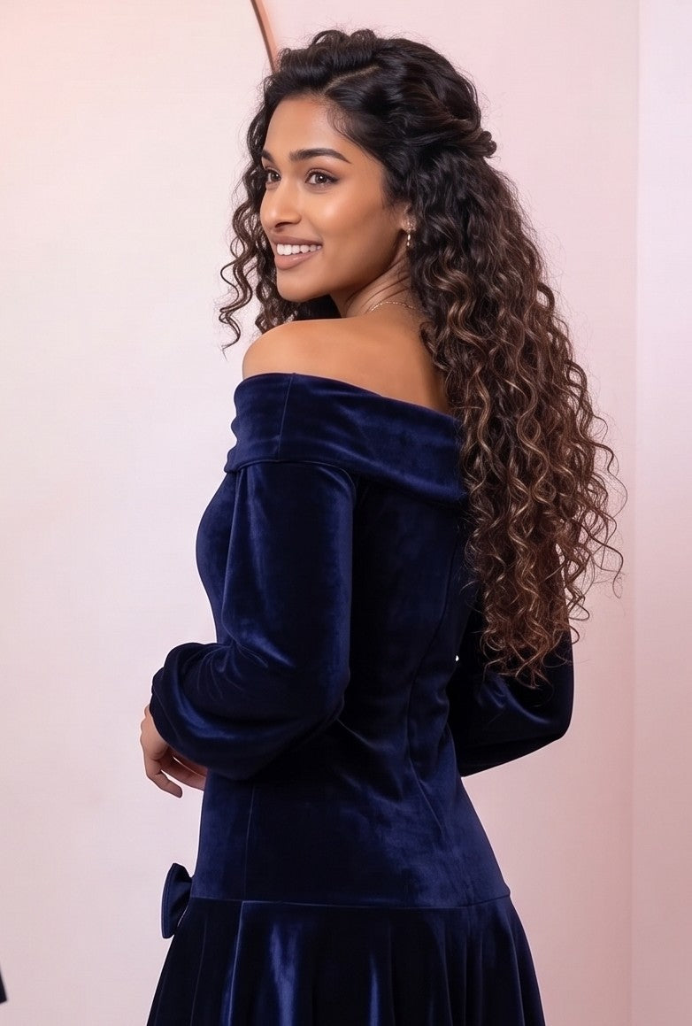 Vestido corto de terciopelo azul marino de corte evasé con escote bardot de hombros descubiertos, mangas largas abullonadas tipo farol y detalle de lazos en cadera y pecho.