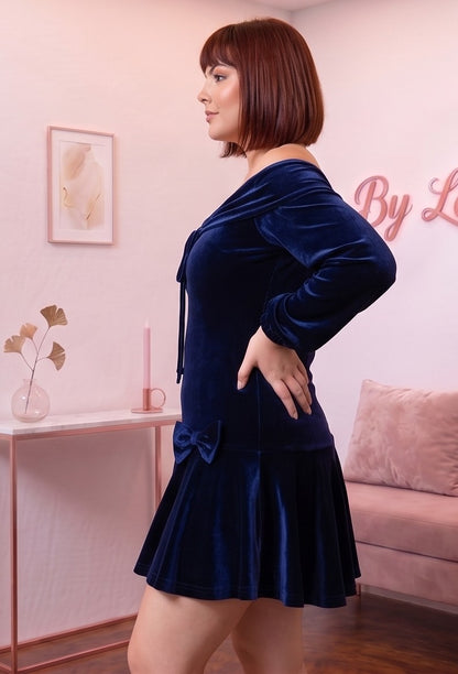 Vestido corto de terciopelo azul marino de corte evasé con escote bardot de hombros descubiertos, mangas largas abullonadas tipo farol y detalle de lazos en cadera y pecho.