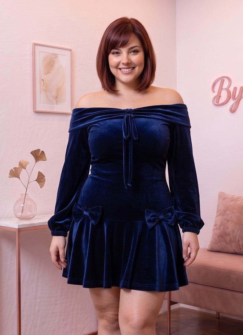 Vestido corto de terciopelo azul marino de corte evasé con escote bardot de hombros descubiertos, mangas largas abullonadas tipo farol y detalle de lazos en cadera y pecho.