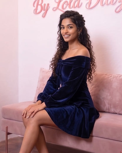 Vestido corto de terciopelo azul marino de corte evasé con escote bardot de hombros descubiertos, mangas largas abullonadas tipo farol y detalle de lazos en cadera y pecho.