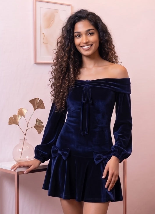 Vestido corto de terciopelo azul marino de corte evasé con escote bardot de hombros descubiertos, mangas largas abullonadas tipo farol y detalle de lazos en cadera y pecho.