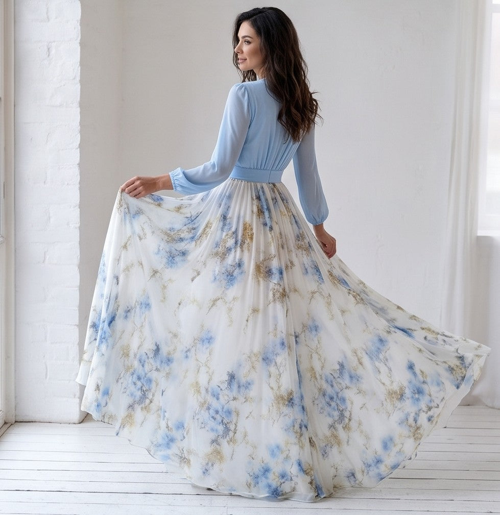 Vestido largo de fiesta para invitada con cuerpo cruzado en gasa azul cielo, escote en V pronunciado, mangas largas abullonadas y falda fluida blanca con estampado floral en tonos azules y dorados.