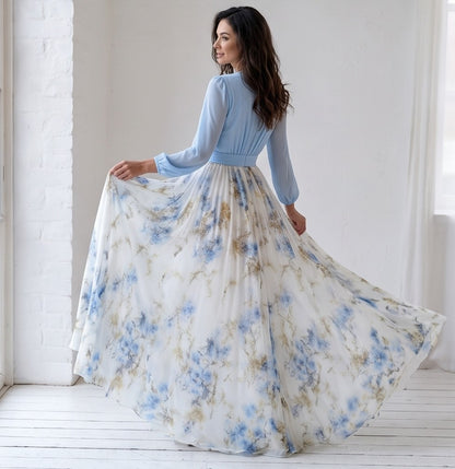 Vestido largo de fiesta para invitada con cuerpo cruzado en gasa azul cielo, escote en V pronunciado, mangas largas abullonadas y falda fluida blanca con estampado floral en tonos azules y dorados.