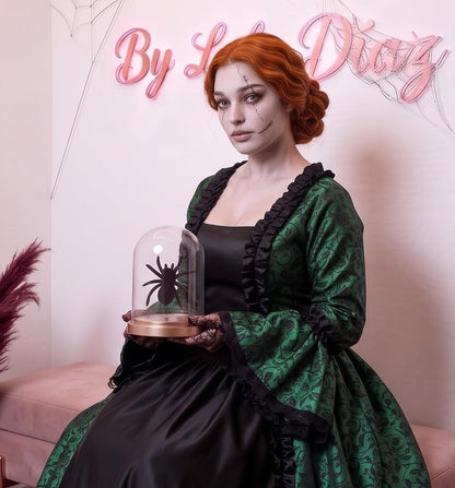 Vestido de época victoriana y corte medieval para mujer en tejido de damasco satinado con estampado floral barroco y panel frontal liso en contraste; presenta escote cuadrado ribeteado con encaje fruncido, mangas largas acampanadas estilo campana, corpiño ajustable tipo corsé en la espalda con lazada y gargantilla a juego. Disponible en cinco variantes de color combinadas con negro: verde esmeralda, morado berenjena, rojo granate, azul petróleo y blanco plateado.