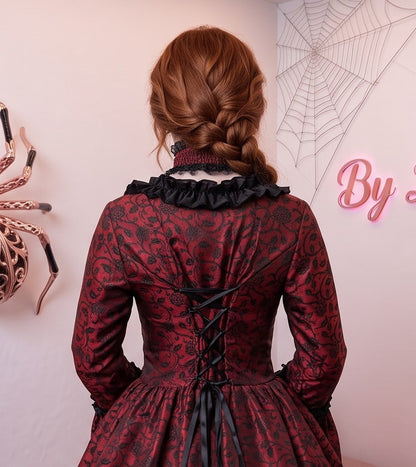 Vestido de época victoriana y corte medieval para mujer en tejido de damasco satinado con estampado floral barroco y panel frontal liso en contraste; presenta escote cuadrado ribeteado con encaje fruncido, mangas largas acampanadas estilo campana, corpiño ajustable tipo corsé en la espalda con lazada y gargantilla a juego. Disponible en cinco variantes de color combinadas con negro: verde esmeralda, morado berenjena, rojo granate, azul petróleo y blanco plateado.