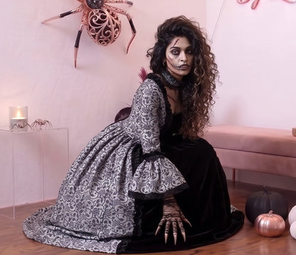 Vestido de época victoriana y corte medieval para mujer en tejido de damasco satinado con estampado floral barroco y panel frontal liso en contraste; presenta escote cuadrado ribeteado con encaje fruncido, mangas largas acampanadas estilo campana, corpiño ajustable tipo corsé en la espalda con lazada y gargantilla a juego. Disponible en cinco variantes de color combinadas con negro: verde esmeralda, morado berenjena, rojo granate, azul petróleo y blanco plateado.