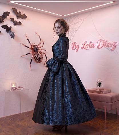 Vestido de época victoriana y corte medieval para mujer en tejido de damasco satinado con estampado floral barroco y panel frontal liso en contraste; presenta escote cuadrado ribeteado con encaje fruncido, mangas largas acampanadas estilo campana, corpiño ajustable tipo corsé en la espalda con lazada y gargantilla a juego. Disponible en cinco variantes de color combinadas con negro: verde esmeralda, morado berenjena, rojo granate, azul petróleo y blanco plateado.